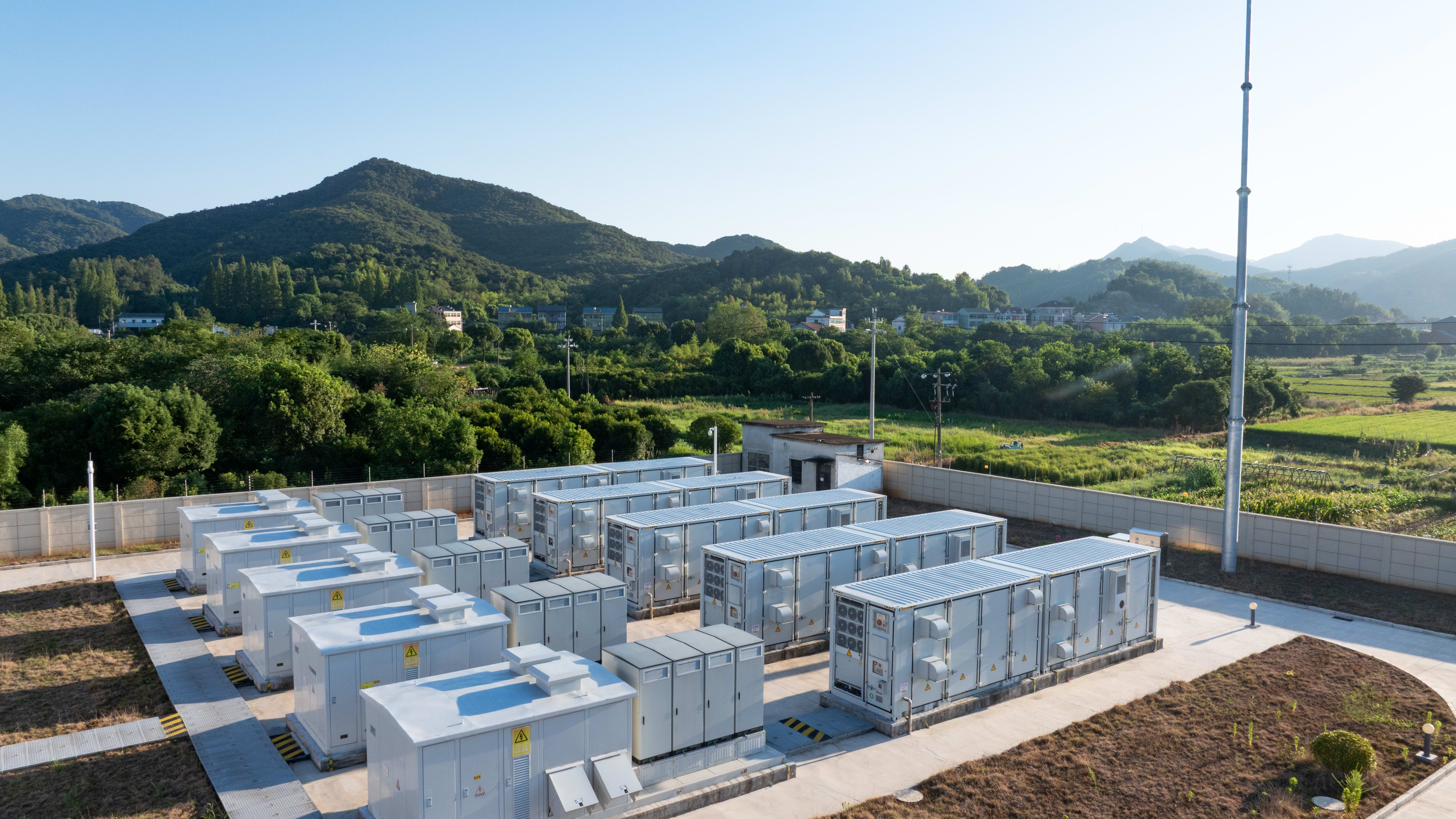 Outdoor battery energy storage system with rows of white units in a rural mountain setting
