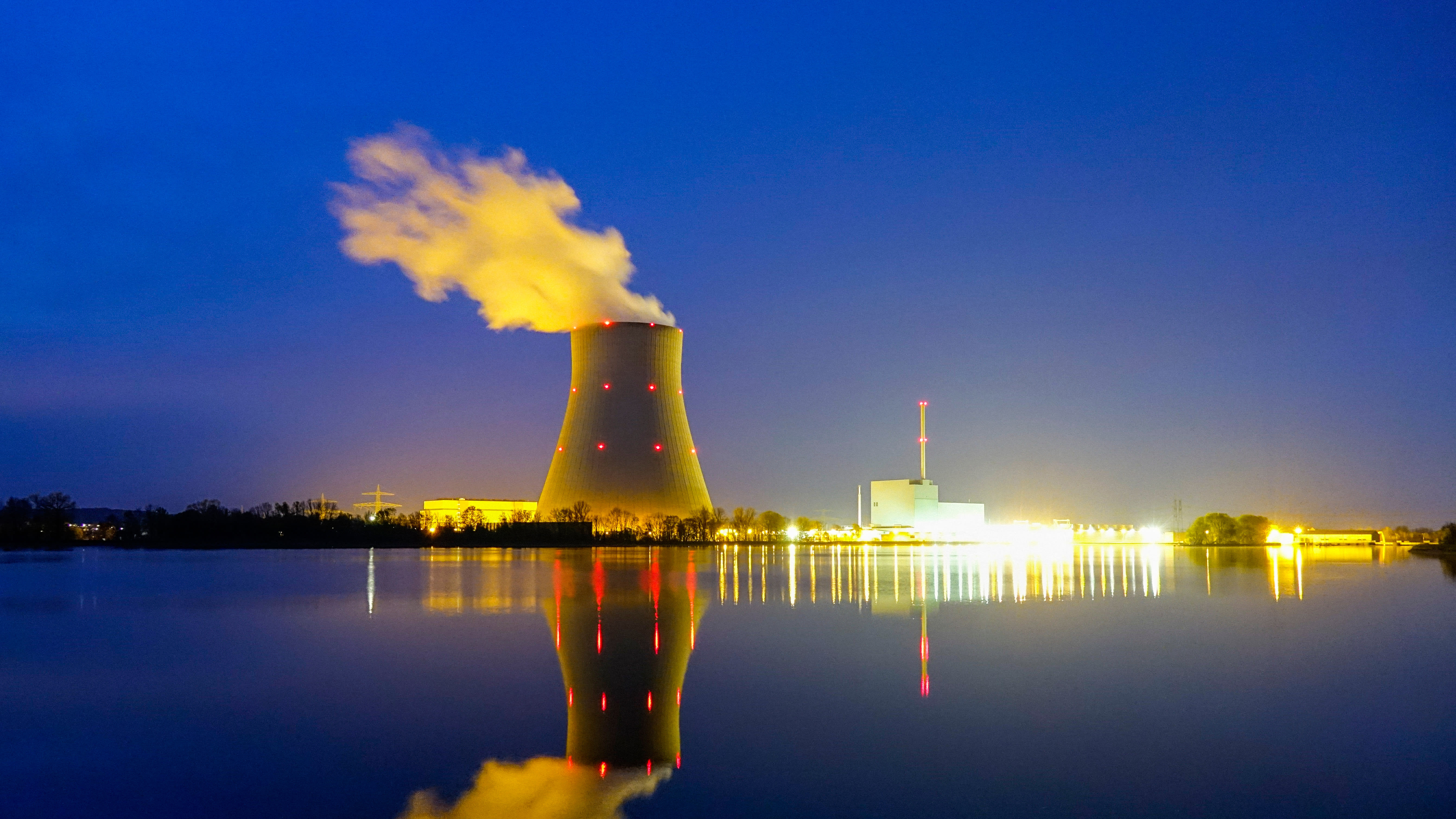 Beleuchtetes Kraftwerk bei Nacht und Spiegelung im Wasser