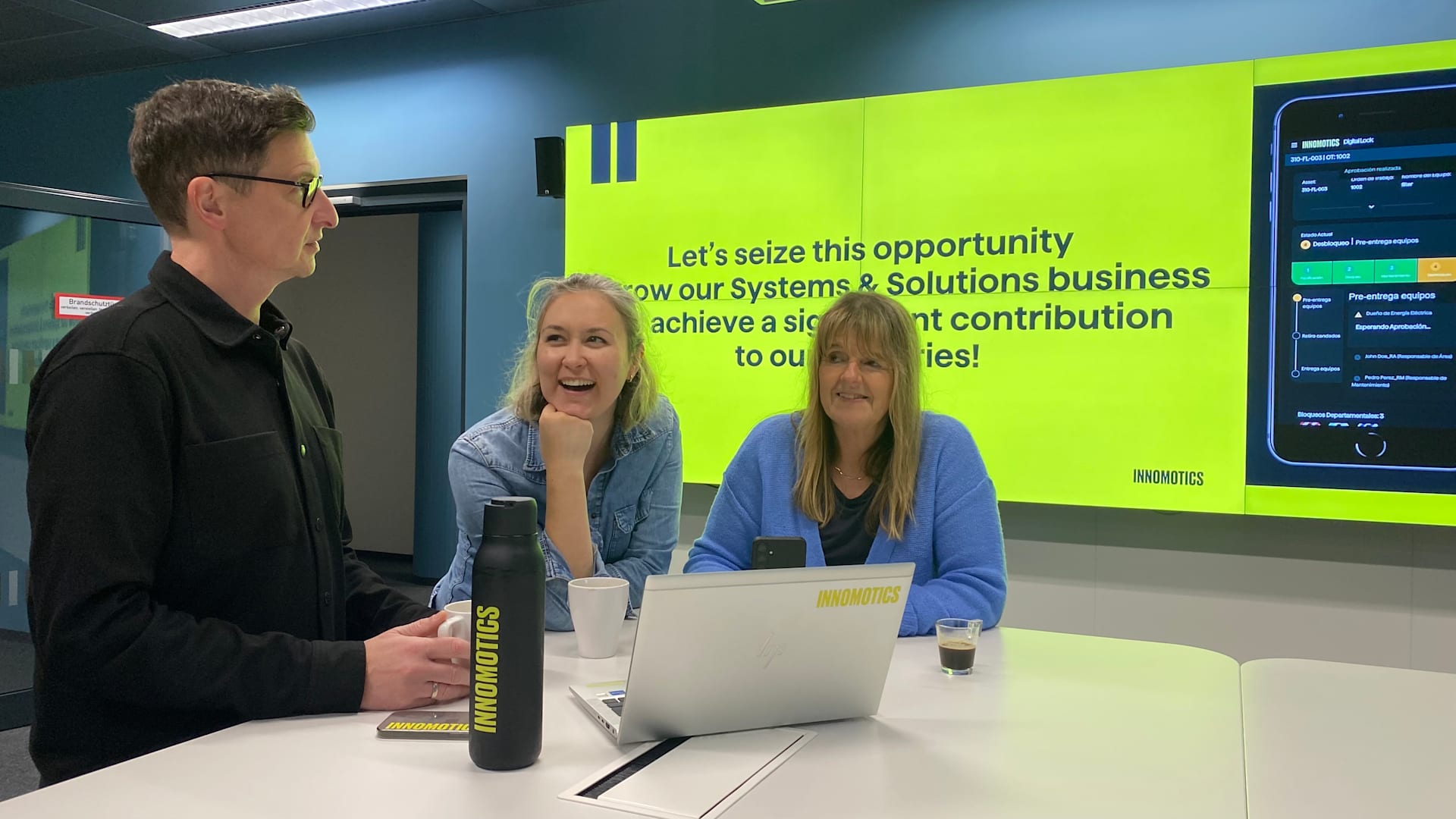 Three colleagues in front of an LED screen happily talking
