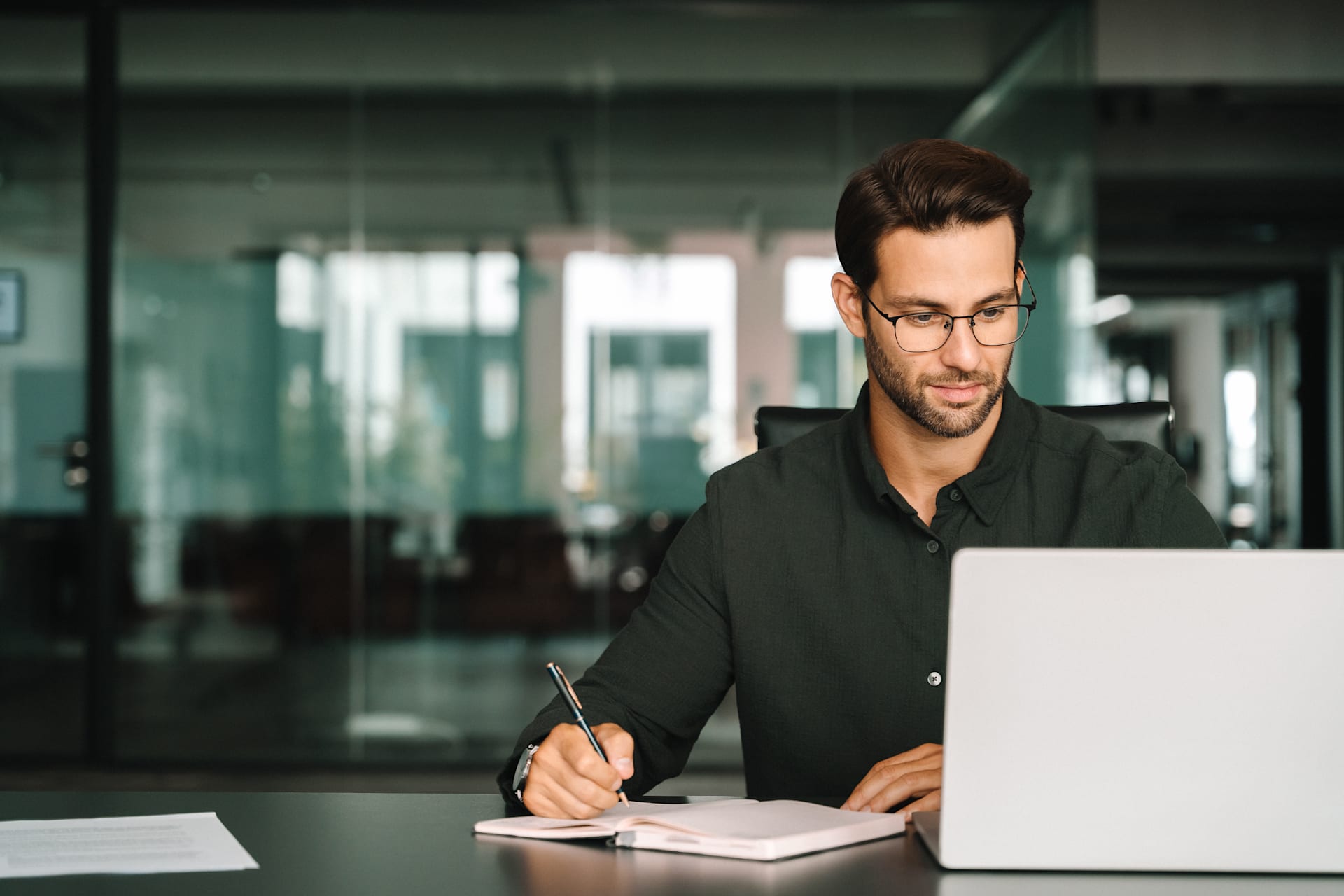Professional businessman with glasses working on laptop and taking notes in a modern office Professional businessman with glasses working on laptop and taking notes in a modern office